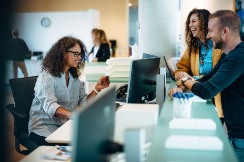 Three office workers sitting around a desk smiling