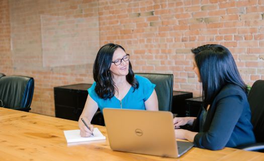 A woman in a teal shirt talking with another woman in a suit jacket.