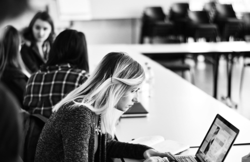young woman looking at laptop at a table with three other young women