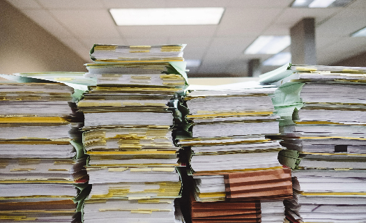 Four piles of stacked folders and documents in an office.