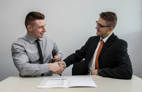 Two men in suits shaking hands over a table with papers on it
