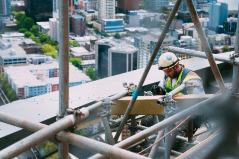 A man at a high-altitude construction site seen focusing on his welding job.