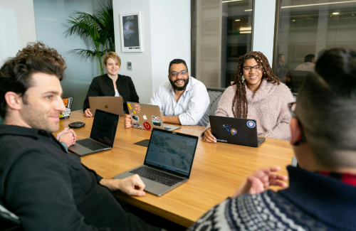 5 people sitting around a table with laptops discussing something