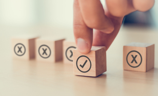 Person selecting a wooden block with a check mark inside a circle with other wooden blocks on the table containing a circle with an "X" on it.