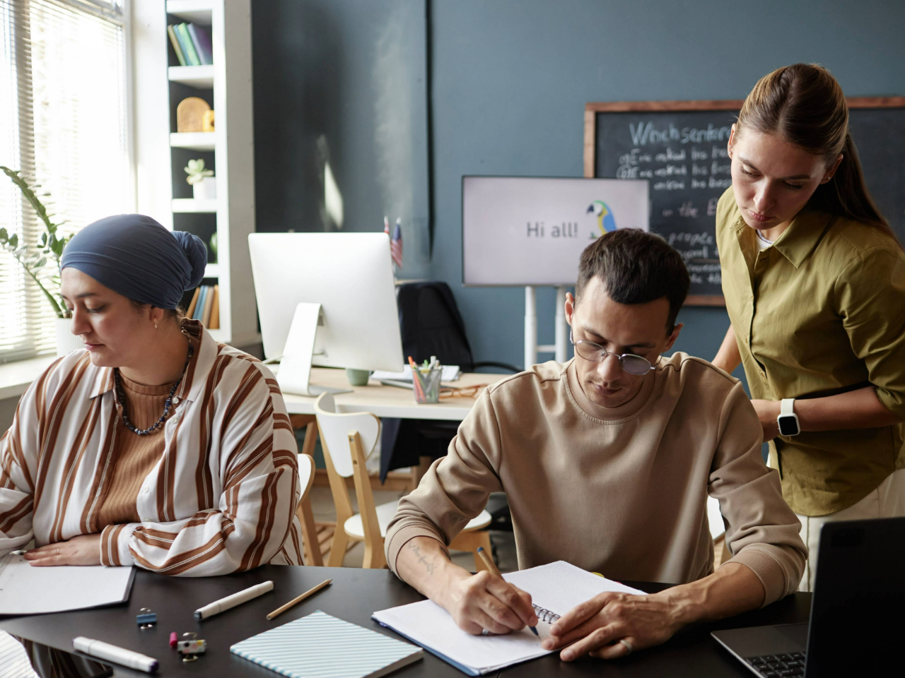 Two adults sitting at a table writing with a teacher observing