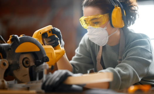 A woman wearing protective gear and using a saw.