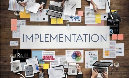 Desk with papers and the word Implementation on a banner