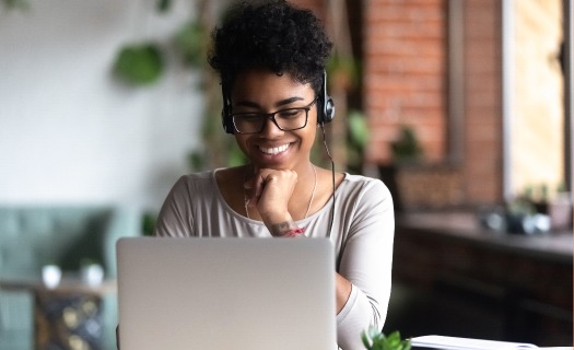 A woman with headphones on sits at a laptop computer smiling. 