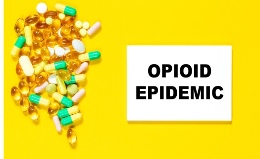 A variety of pills beside a sign that reads OPIOD EPIDEMIC.
