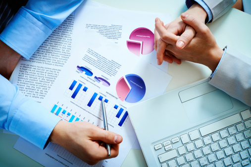 Over view of two business people's hands as they look at charts next to a laptop keyboard