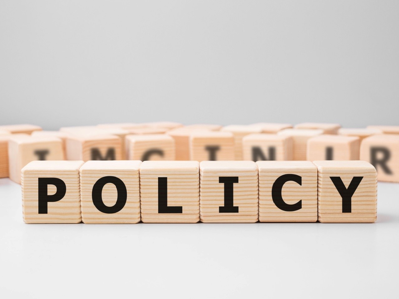 Word POLICY made with wood building blocks. Other block letters are visible in the background, but blurred.