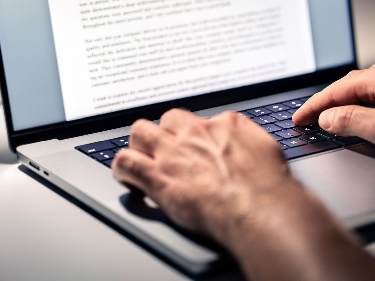 Closeup photo of hands typing on laptop with part of the screen visible showing paragraphs of text.