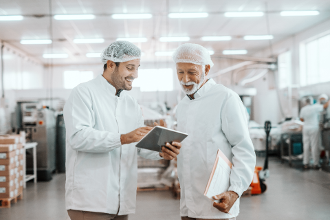 Young supervisor showing the results on his tablet to an older worker in a food plant