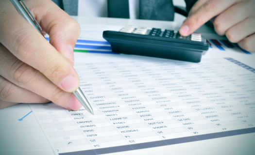 person making notes on a spreadsheet and using a calculator