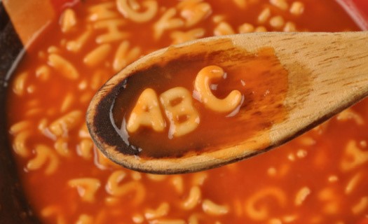 The letters ABC made out of noodles on a wooden spoon above a pot of alphabet soup