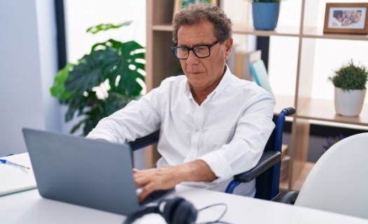 Older man working from home in wheelchair at laptop on desk