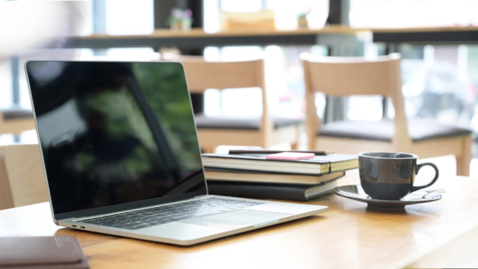 A laptop on a table with books and a cup on the side