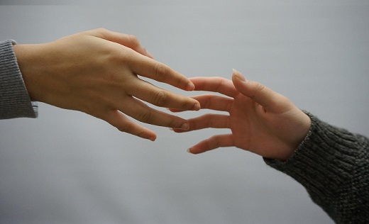 Two reaching hands touching fingertips