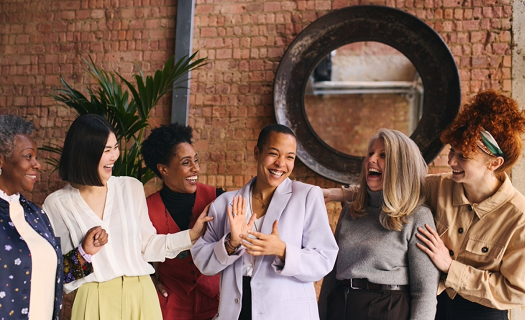 Diverse group of women standing in a modern space, clapping and celebrating