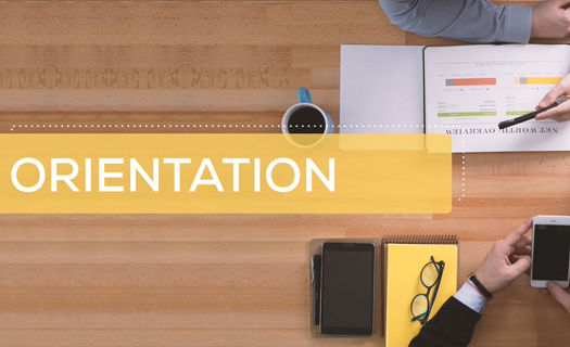 The word ORIENTATION over a photo that is an aerial view of an office desk with two people working at it.