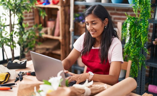 Woman using a laptop on the counter of a modern looking florist or plant shop.