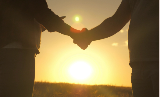 Two people shaking hands with a sunset in the background.