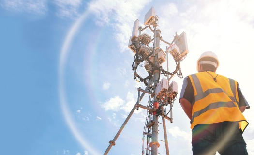 Worker looking up at a cell tower against a blue sky