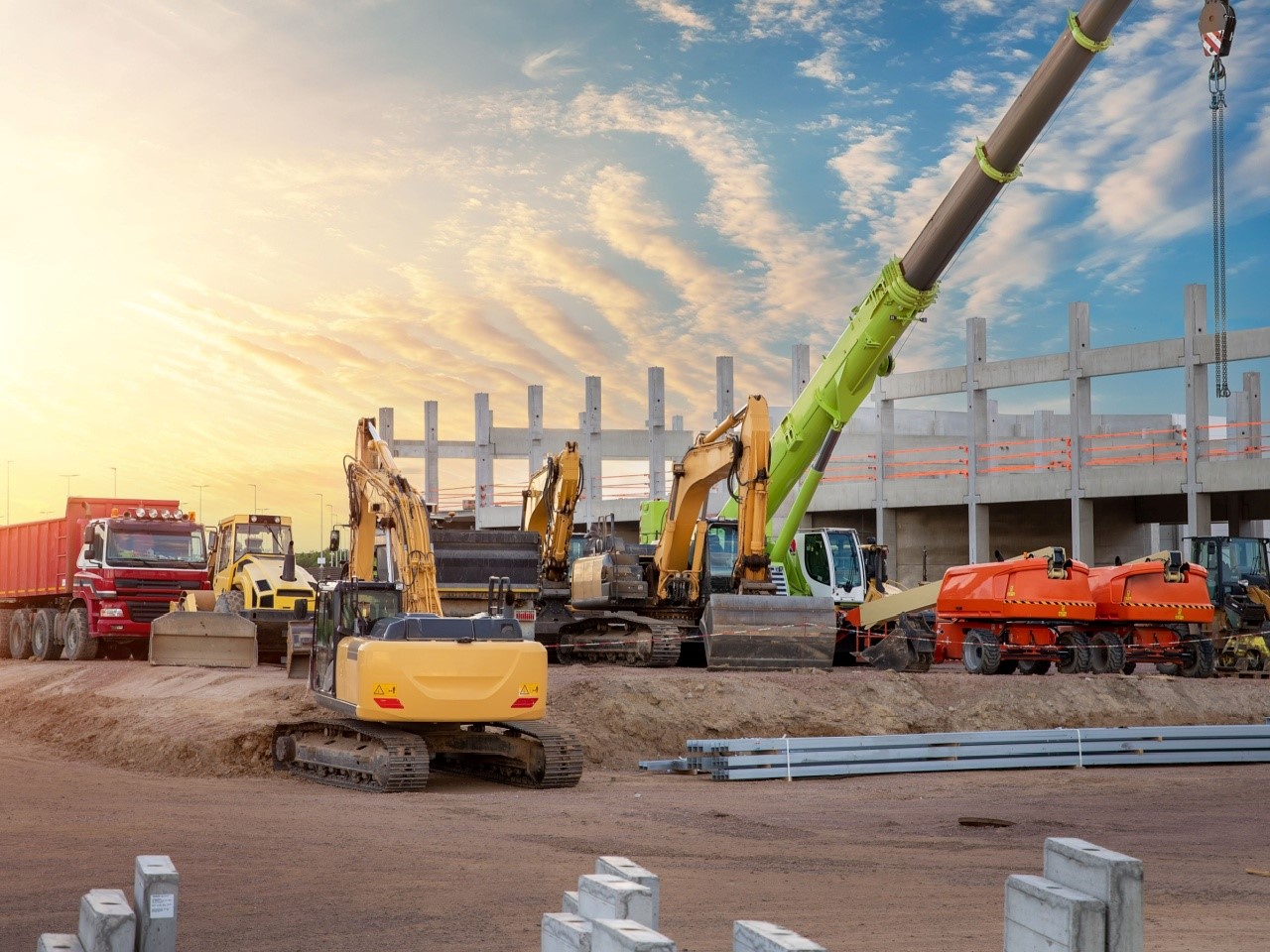 Many different multiclored colorful heavy industrial machinery equipment at construction site parking area against warehouse building city infrastructure development. Commercial vehicles rental sale