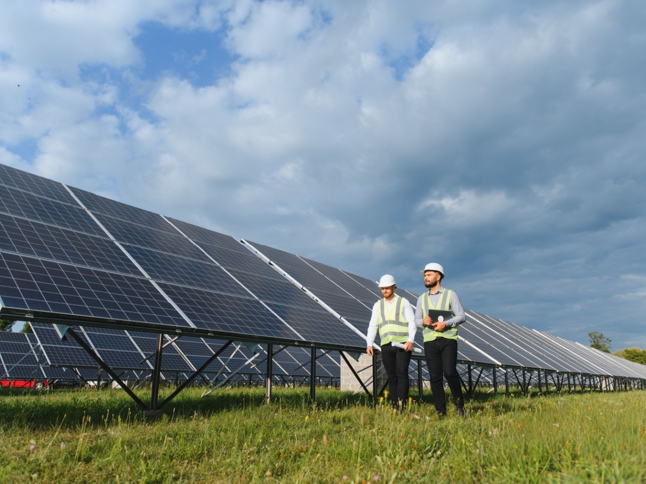 Two engineers in safety gear inspecting solar panel array in a field, symbolizing renewable energy, sustainability, and solar technology